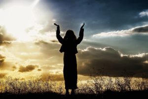 woman raising hands beneath sunlit sky